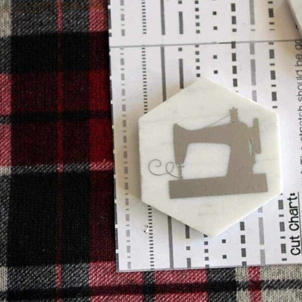 A hexagon tile with a sewing machine decal holding a pattern on fabric.